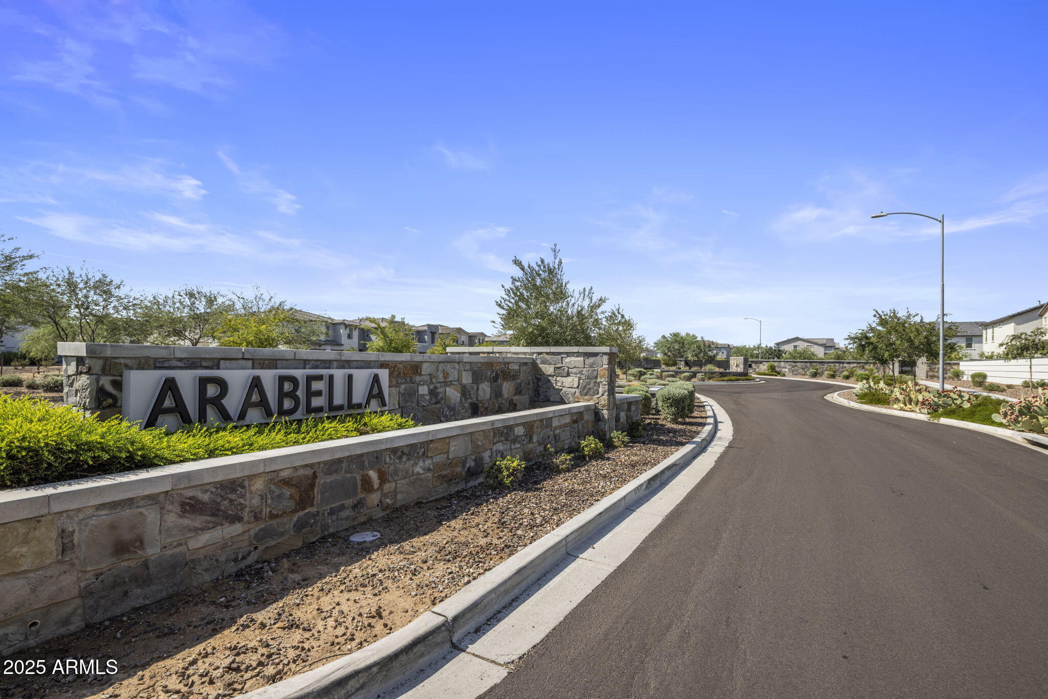 Arabella community entrance with a stone sign wall beside a landscaped, curving road.