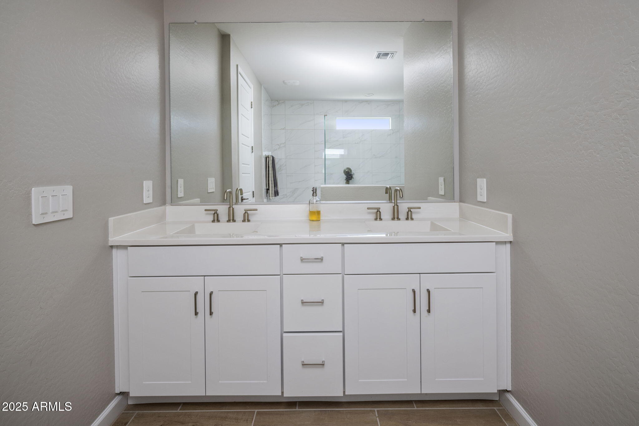 Bathroom vanity with two sinks and a large mirror reflecting a marble-look tiled shower.