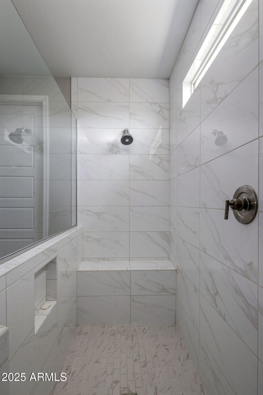 Walk-in shower with marble-look tile, glass enclosure, built-in bench, and high window.