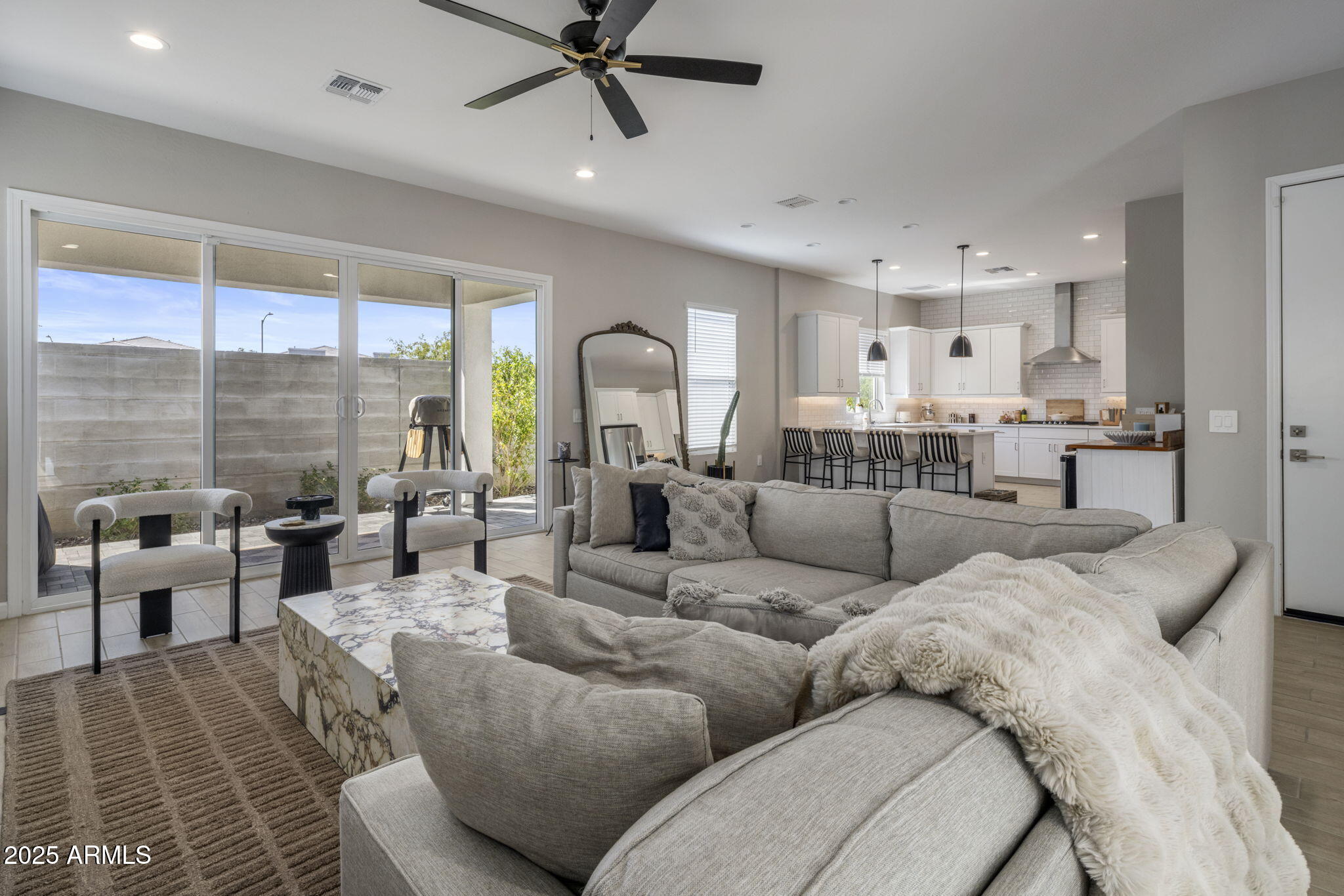 Furnished living room with a gray sectional, open kitchen, and sliding doors to a walled patio.