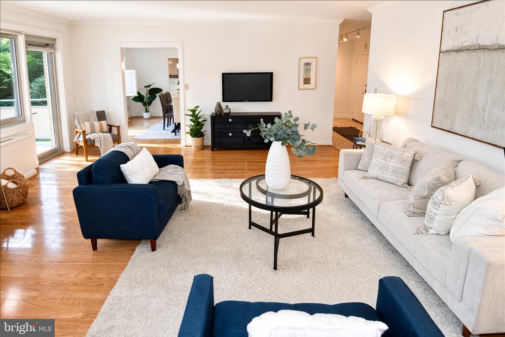 Living room with a white sofa, navy armchairs, hardwood floors, and a wall-mounted television.