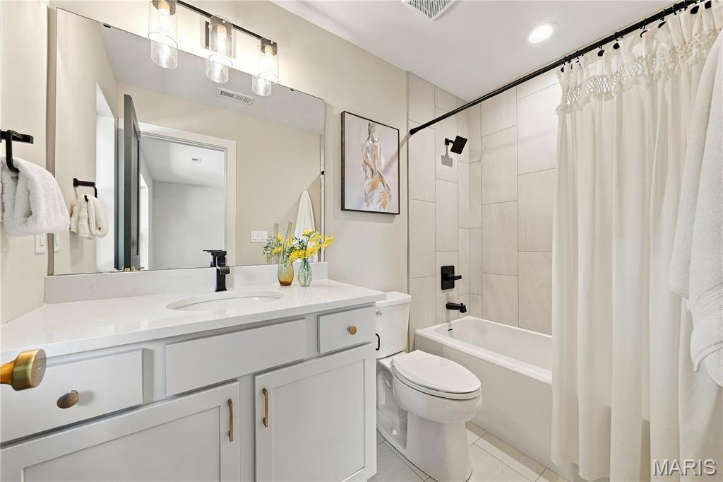 Bathroom with a white vanity, large mirror, and tiled tub-shower behind a curtain.