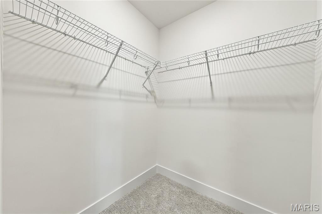 Empty walk-in closet with wire shelving along two walls and light carpet.