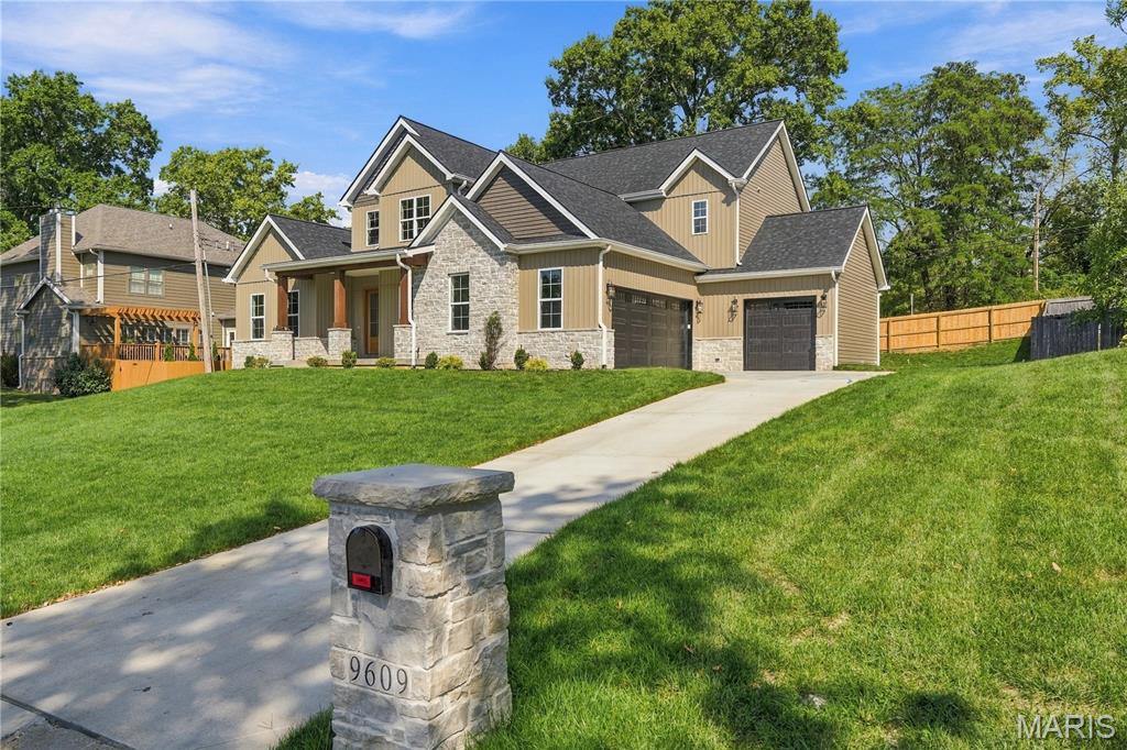 Two-story tan home with stone accents and two garages, viewed from the driveway beside a stone mailbox.