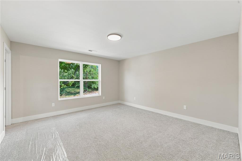 Empty carpeted room with neutral walls and a large window overlooking trees.
