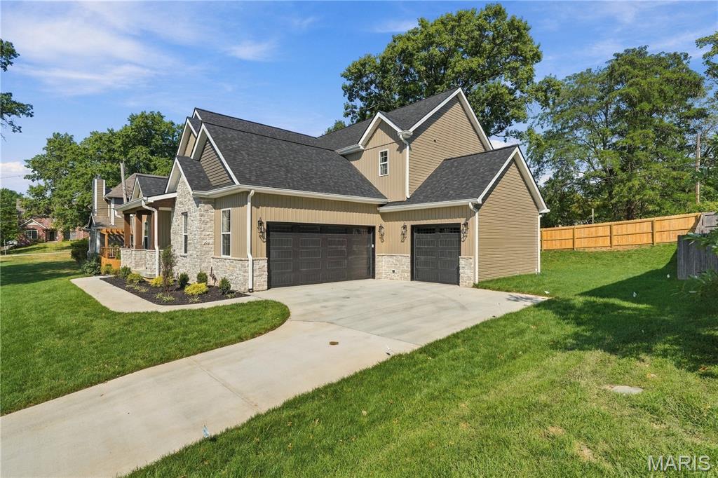 Front exterior of a tan-and-stone home with dark garage doors, a broad driveway, and fenced lawn.