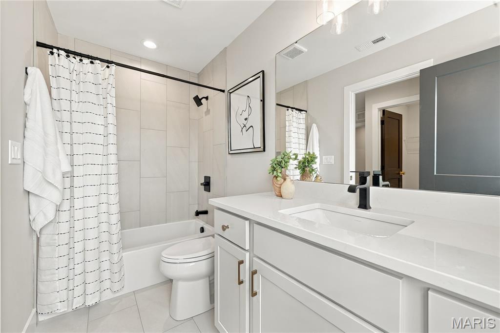 Bathroom with white vanity, large mirror, tiled tub and shower, and striped curtain.