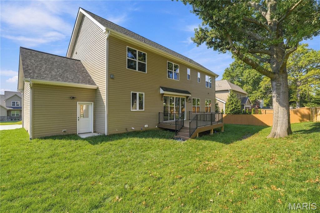 Two-story olive-sided house with a raised deck, broad lawn, mature tree, and wooden privacy fence.