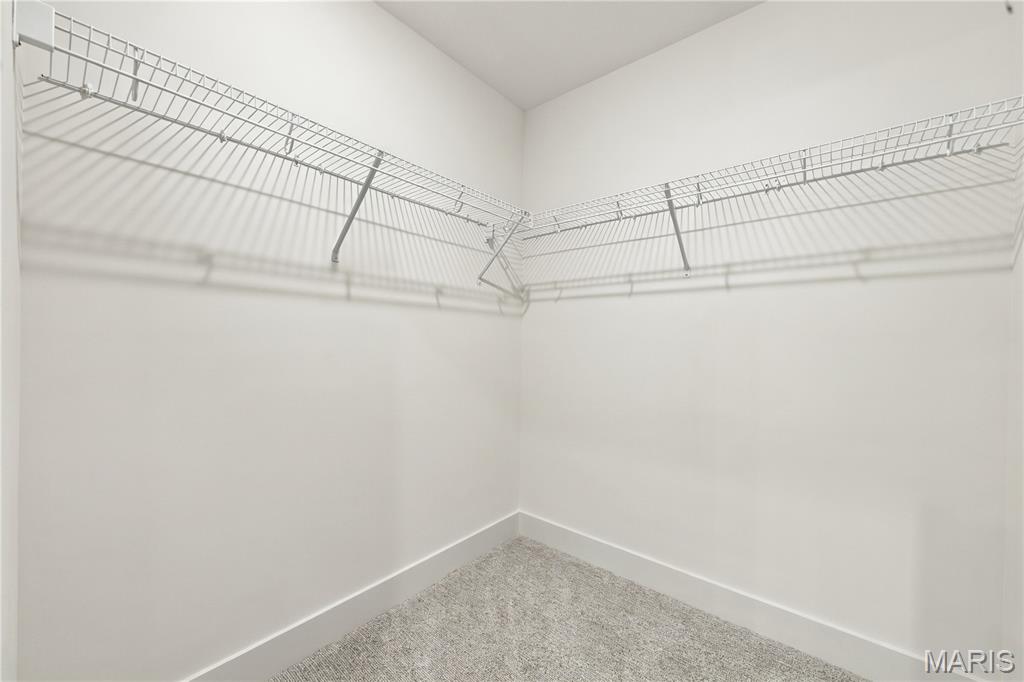 Empty walk-in closet with wraparound wire shelving and gray carpet.