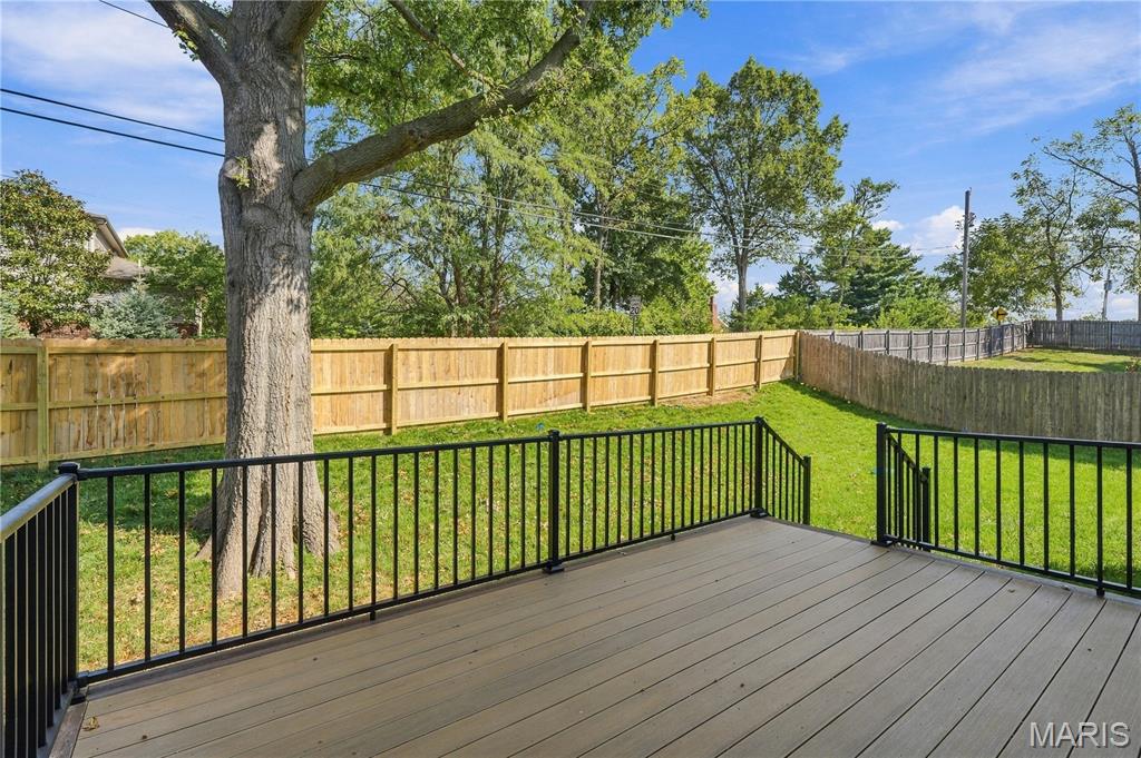 Raised deck with black railings overlooking a fenced lawn and large shade tree.