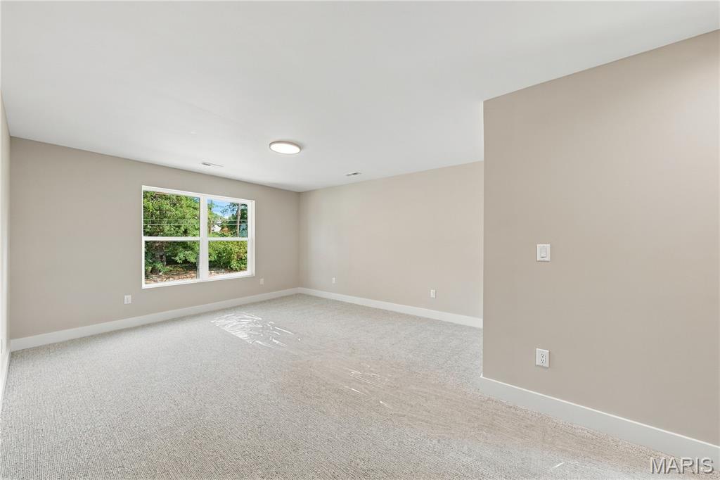 Empty carpeted room with beige walls, a large window, and trees outside.