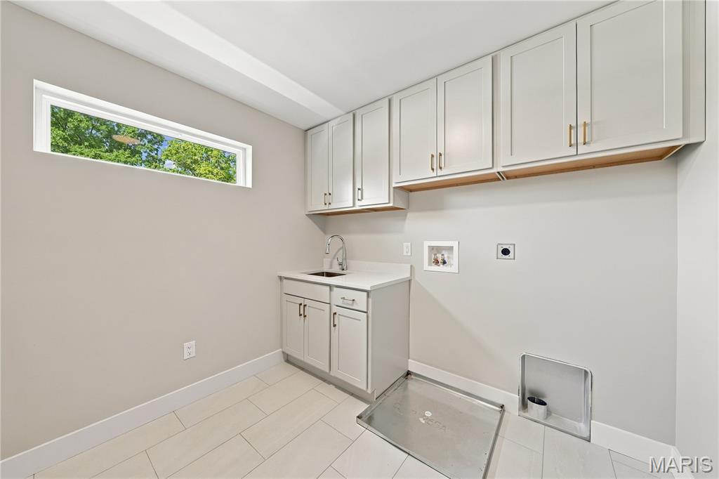 Utility room with white cabinets, a sink, and a metal wash pan on the tiled floor.
