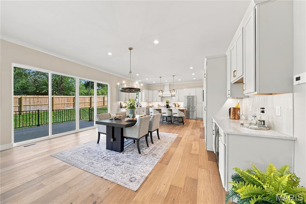Open-plan kitchen and dining area with white cabinetry, wood floors, and wide doors to a fenced deck.