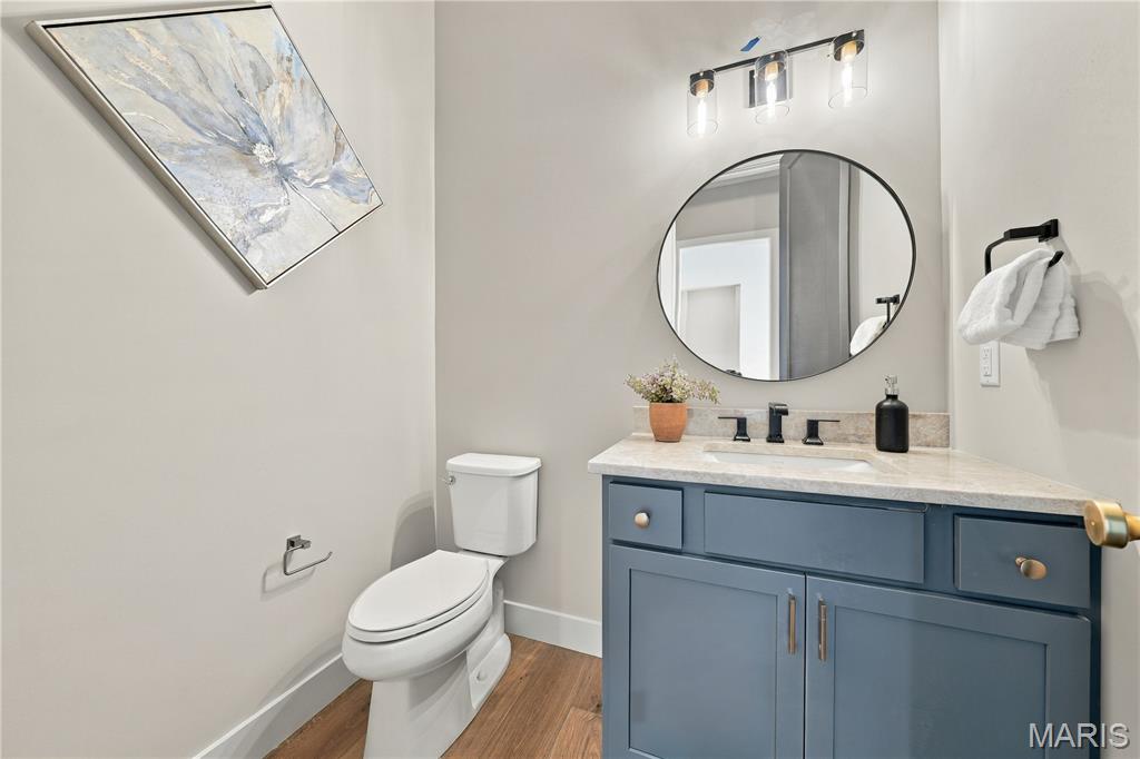 Powder room with a blue vanity, round mirror, white toilet, and wood-look flooring.