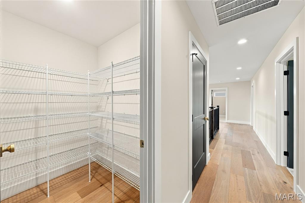 Walk-in closet with white wire shelving and wood flooring beside a bright hallway.