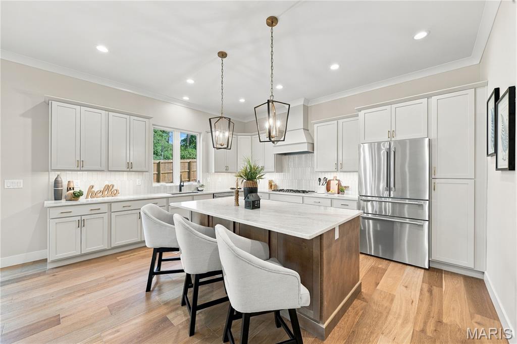 Kitchen with a large island, three upholstered stools, white cabinets, and stainless steel appliances.