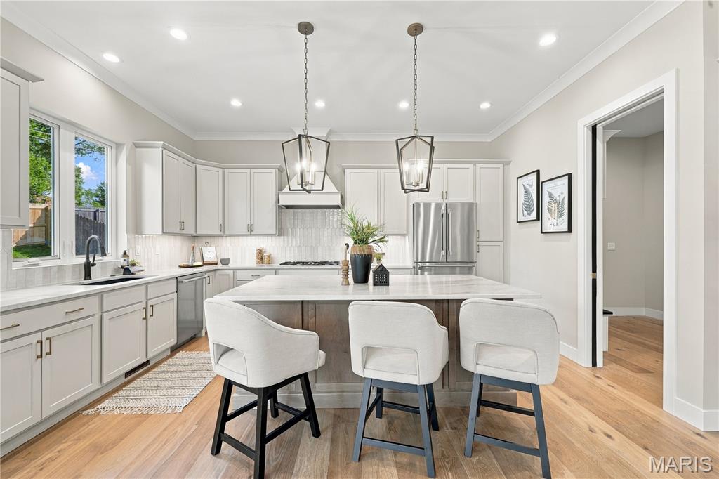 Bright kitchen with a large island, three upholstered stools, white cabinets, and stainless steel appliances.