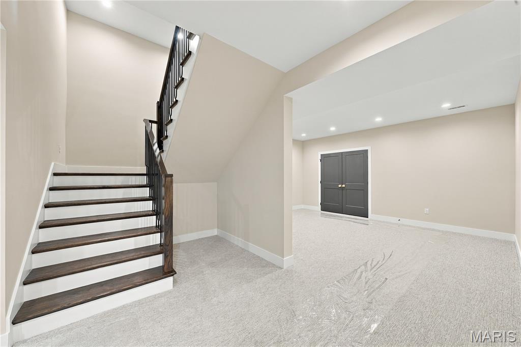 Carpeted room with a dark wood staircase, black railing, and double doors.