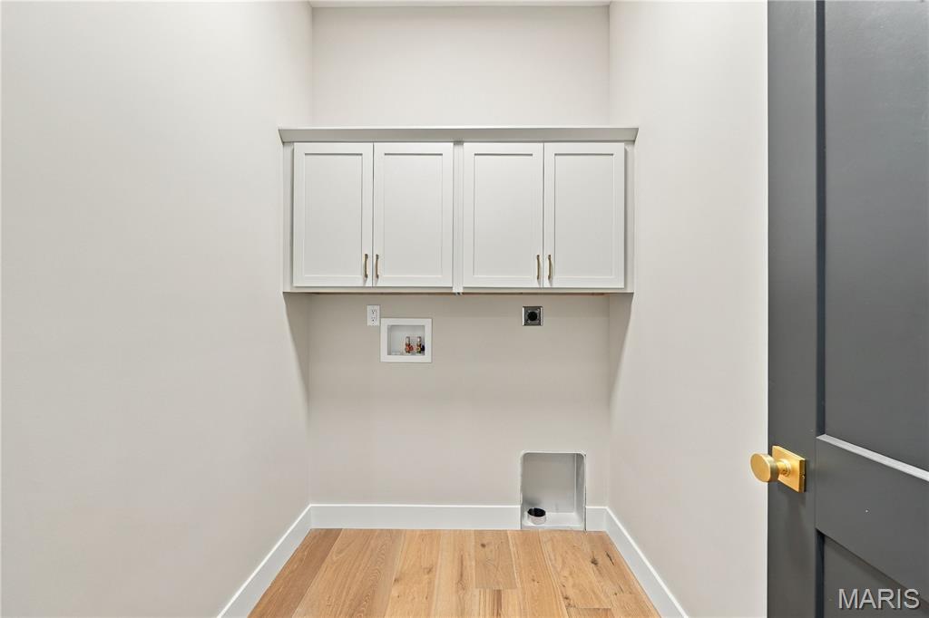 Vacant laundry room with white cabinets, appliance hookups, and light wood flooring.
