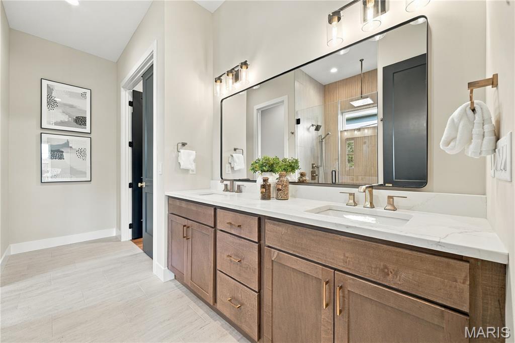 Bathroom with a long wood vanity, double sinks, large mirror, and tiled shower.
