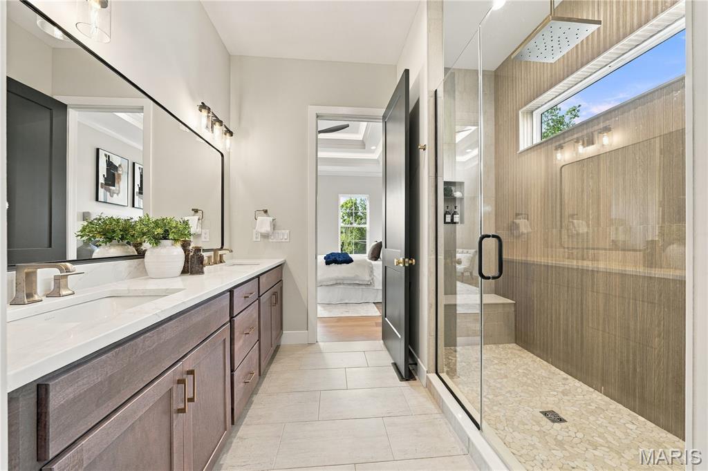 Bathroom with a long double vanity and glass walk-in shower featuring wood-look tile.