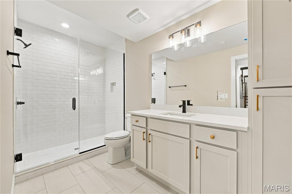 Renovated bathroom with a glass subway-tile shower and white vanity with gold hardware.