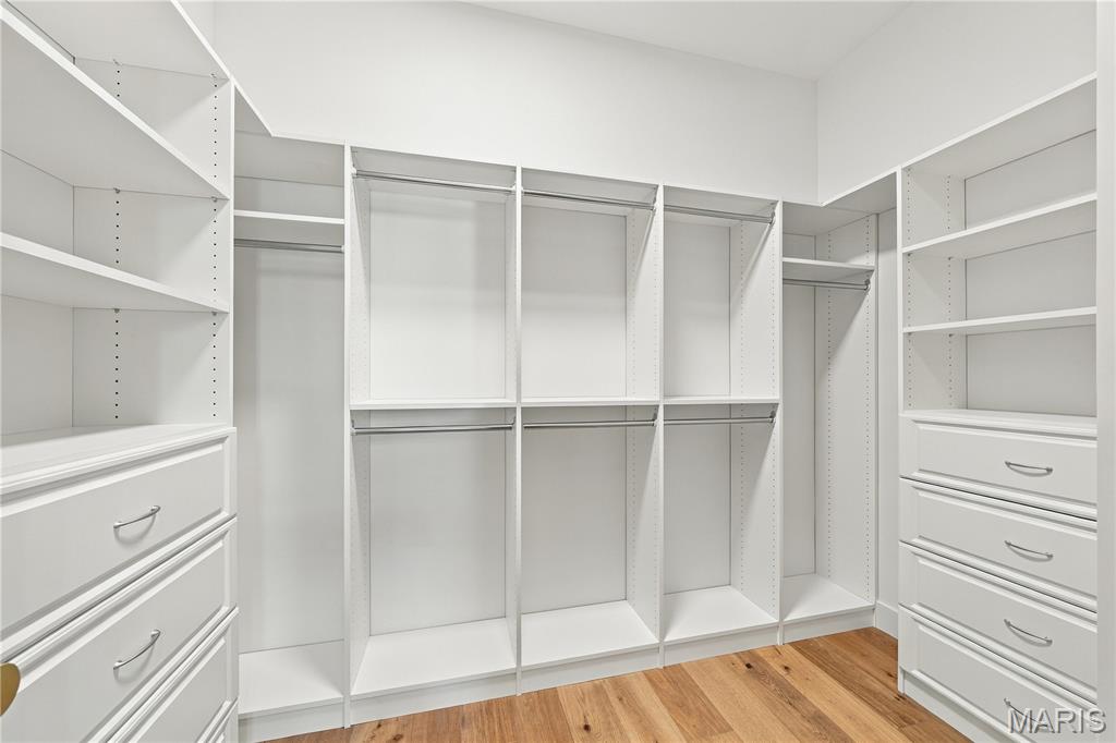Walk-in closet with white built-in shelving, hanging rods, and drawers over a wood floor.