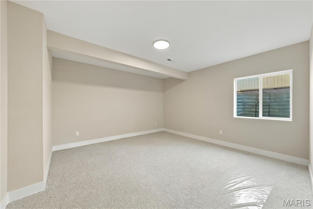 Empty carpeted room with beige walls, a window, and a broad ceiling soffit.