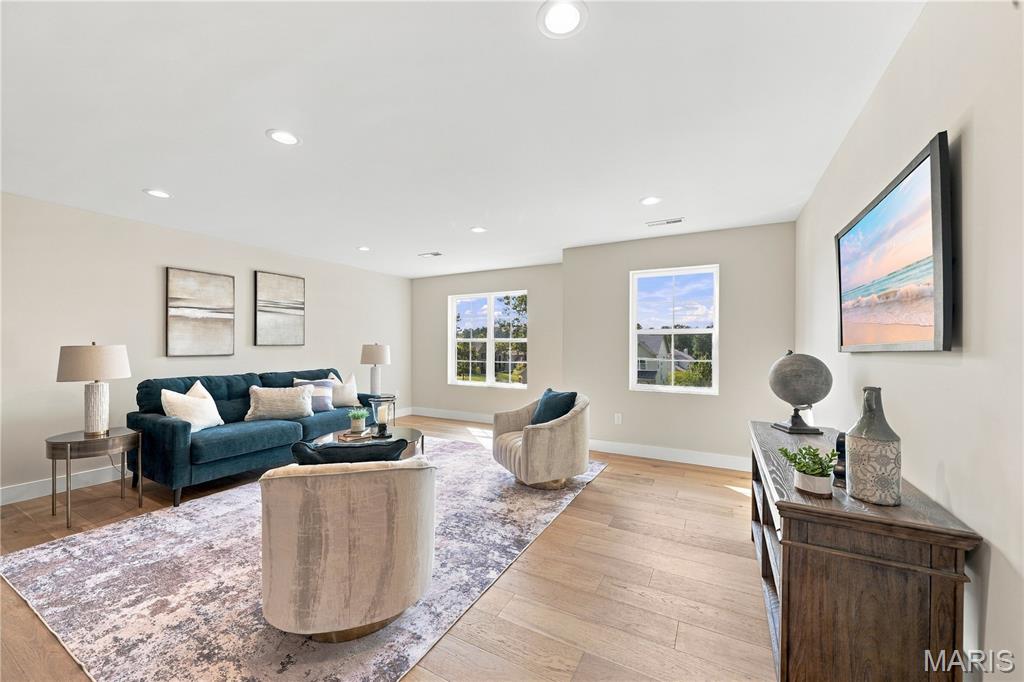 Living room with a blue sofa, pale armchairs, patterned rug, and large windows.