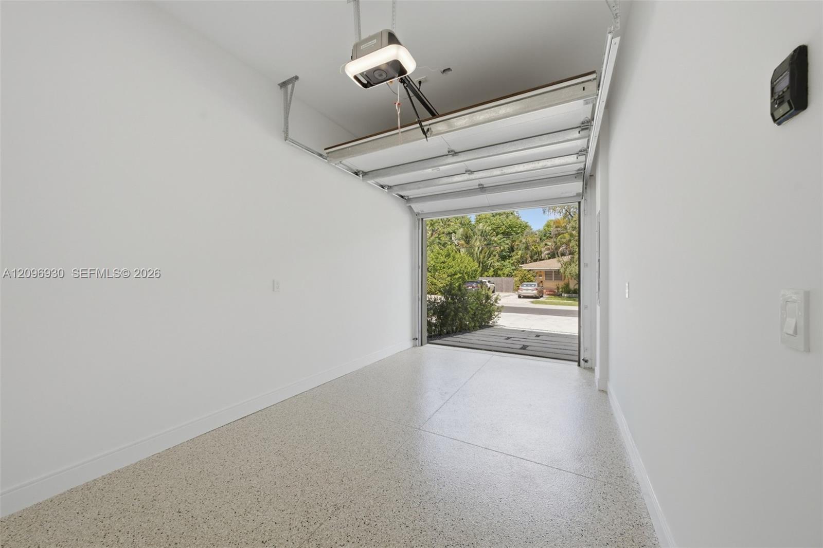 Empty garage with terrazzo floor and open overhead door facing a leafy street.