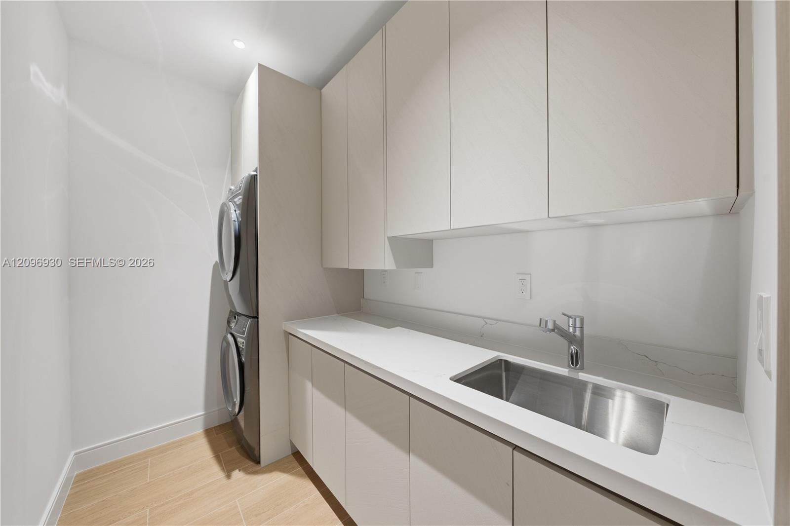 Modern laundry room with stacked washer and dryer, built-in cabinets, and a countertop sink.