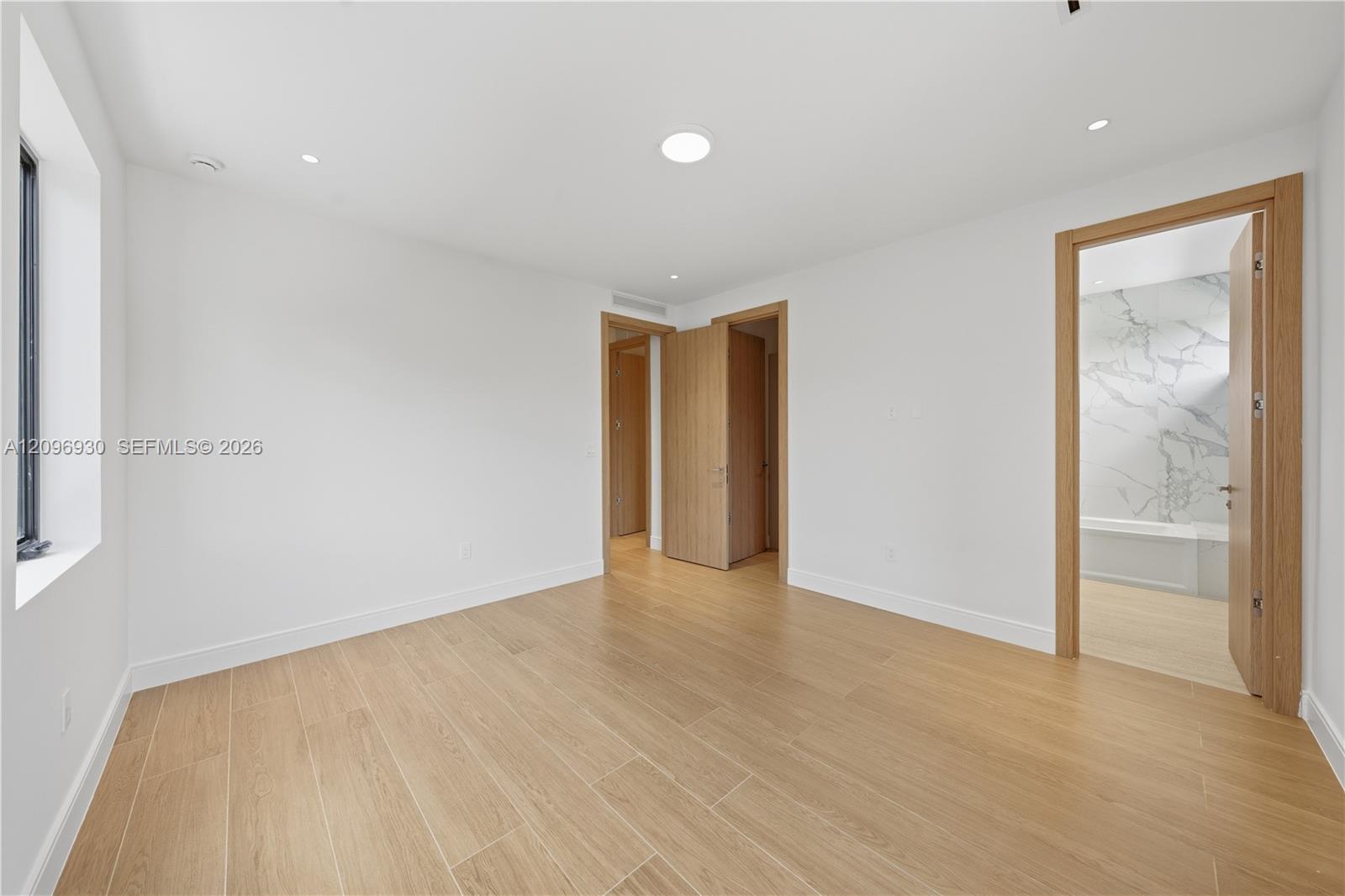 Empty room with light wood-look tile flooring and an open doorway to a marble-accented bathroom.