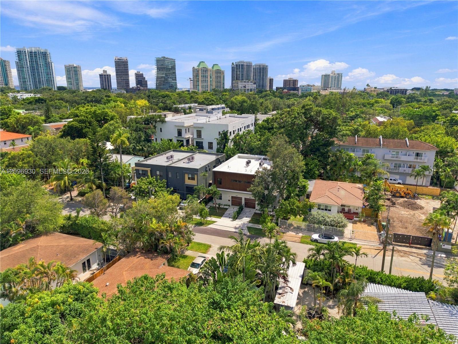 Aerial view of leafy Miami homes with a high-rise skyline in the distance.