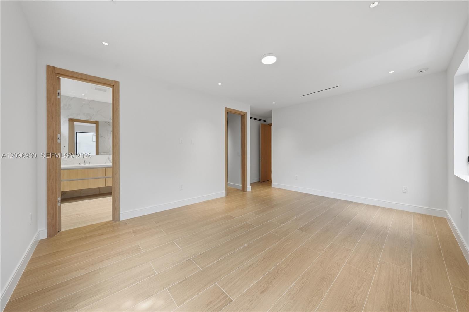 Vacant bedroom with wood-look tile flooring and a bathroom vanity visible through the doorway.