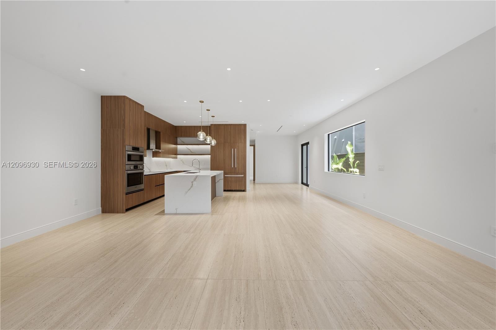 Vacant open-plan interior with a walnut kitchen, white stone island, and pale tile flooring.