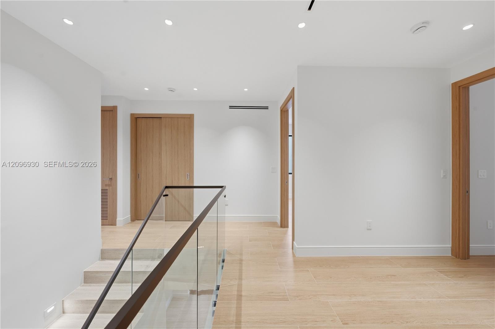 Vacant interior landing with pale tile floors, wood doors, and a glass stair railing.