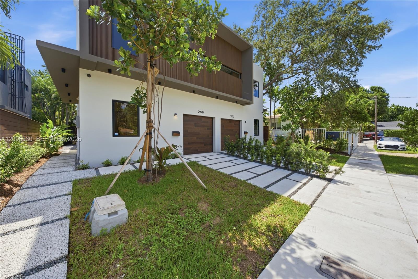 Modern two-story home with white walls, wood-clad upper level, two garage doors, and landscaped frontage.
