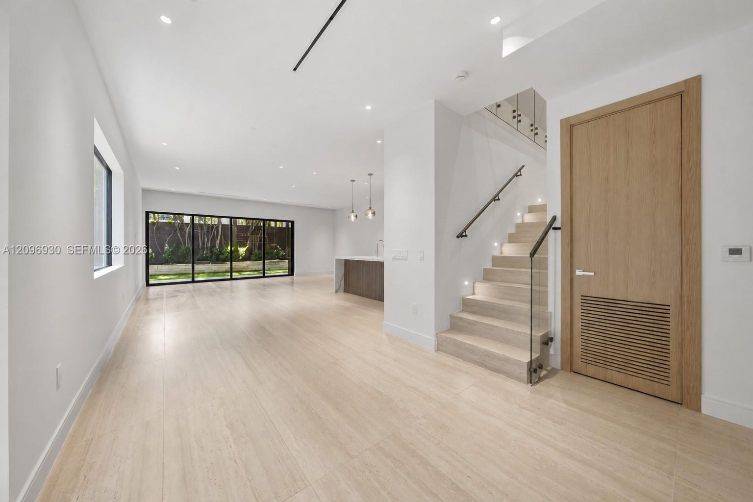 Open living area with pale stone floors, glass-railed staircase, and courtyard-facing sliding doors.