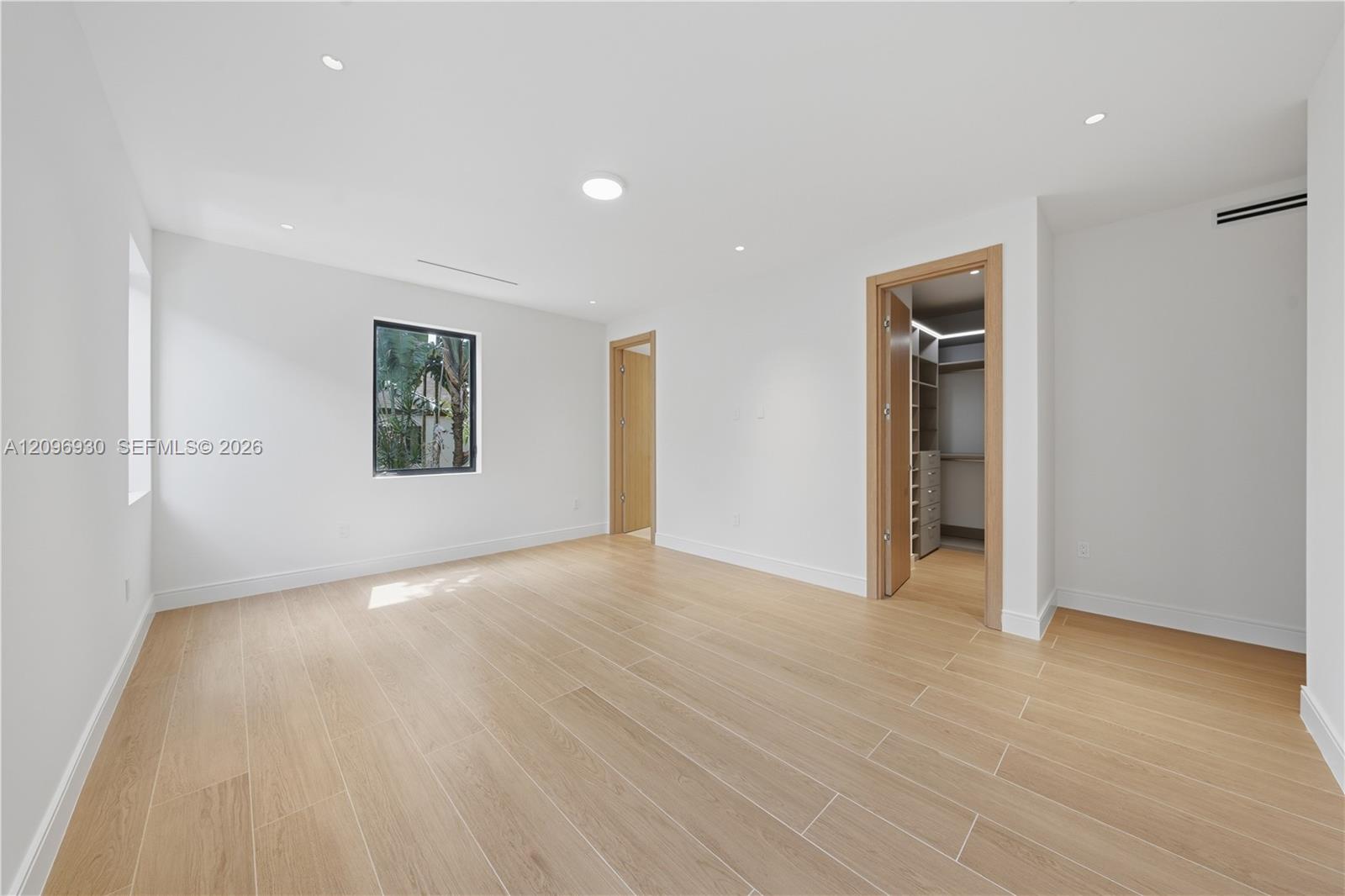 Vacant bedroom with pale tile floors, a garden-view window, and an open walk-in closet.