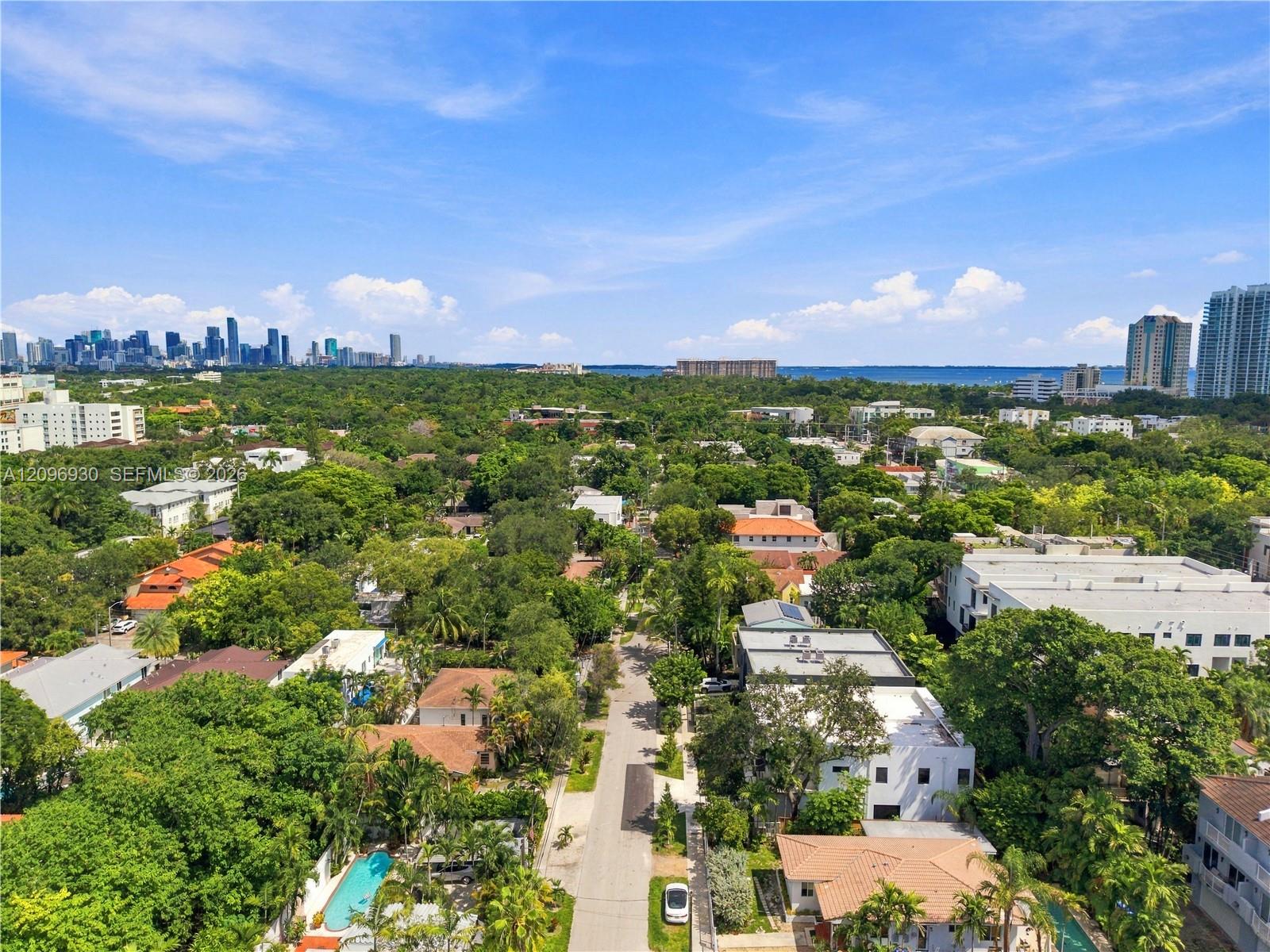 Aerial view over a leafy Miami neighborhood toward the downtown skyline and Biscayne Bay.