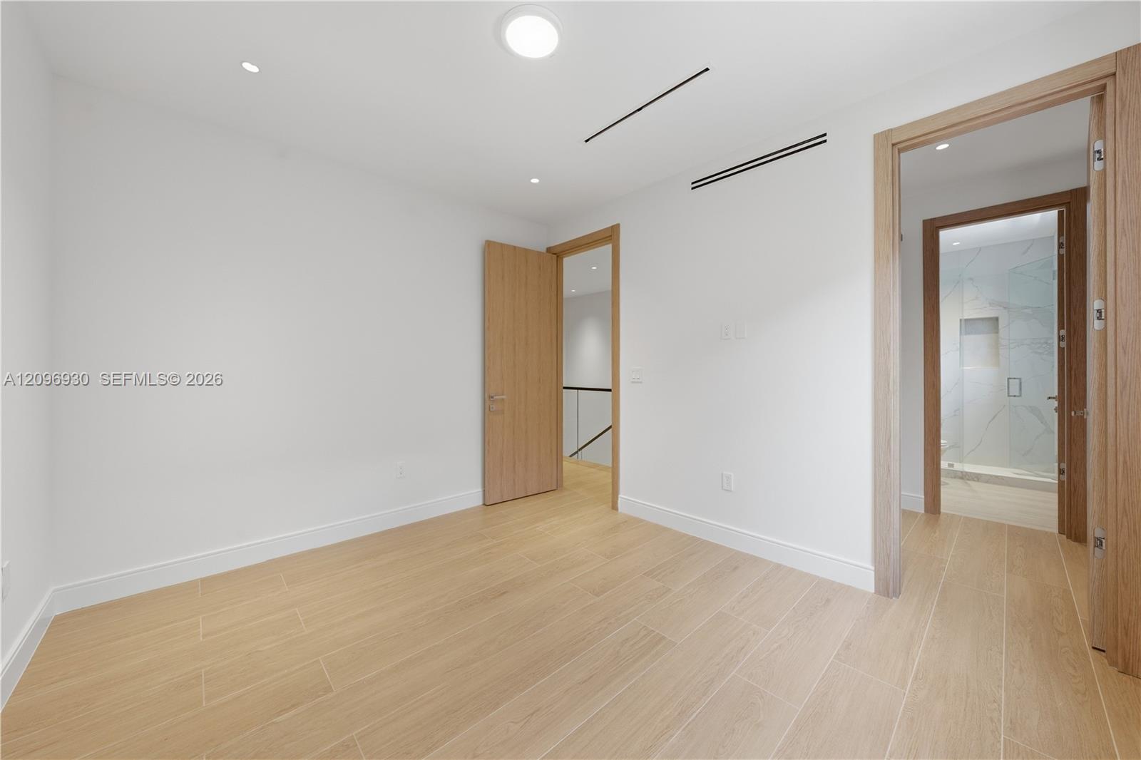 Empty room with pale wood-look tile floors and a doorway to a bathroom with a glass shower.