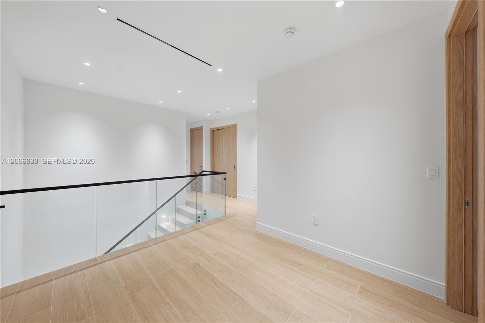 Unfurnished landing with light wood-look tile floors and a glass railing around the staircase.