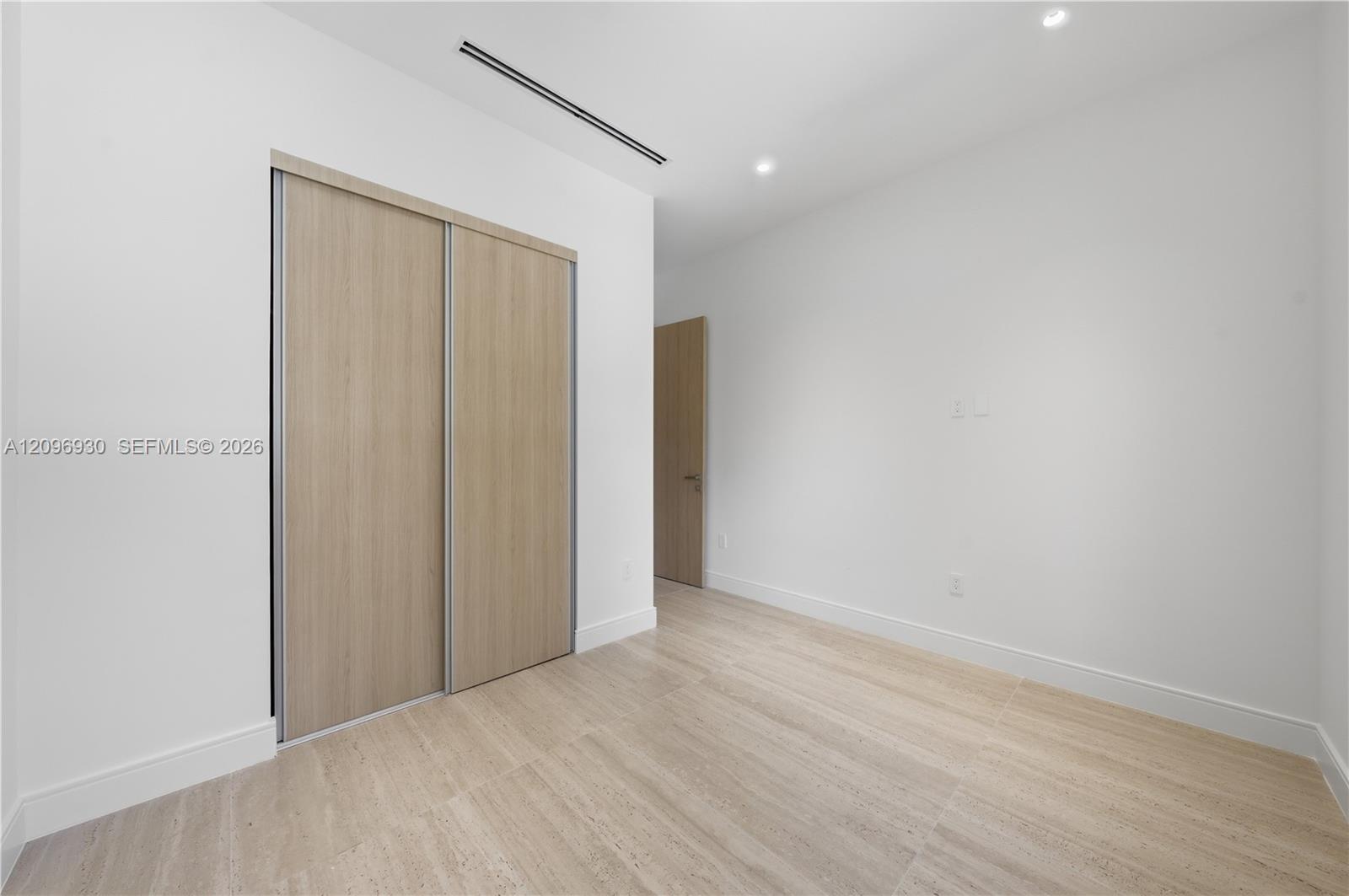 Empty bedroom with a large light-wood sliding closet and pale tile flooring.