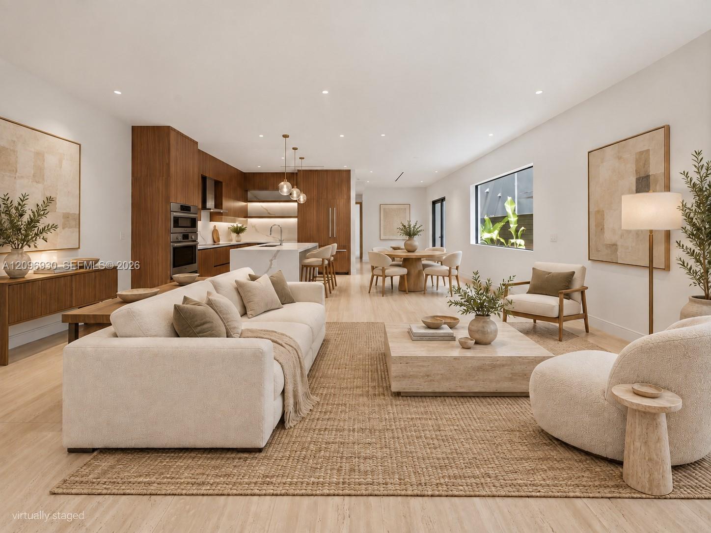 Open-plan living room with white sectional, warm wood kitchen cabinetry, marble island, and round dining table.
