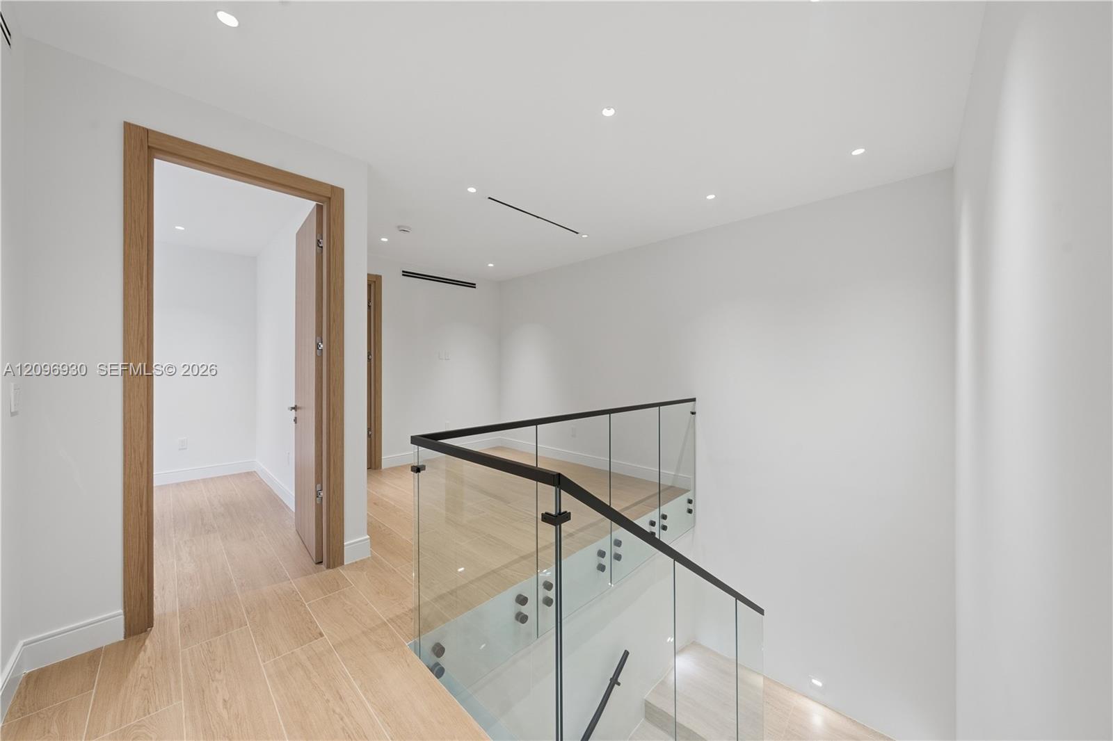 Modern upstairs landing with light tile floors and a glass stair railing.