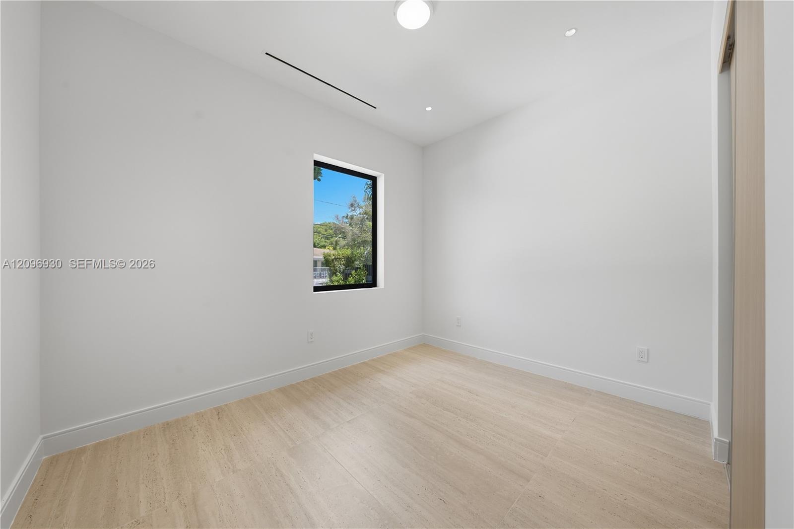 Vacant room with pale tile flooring and a black-framed window overlooking trees.