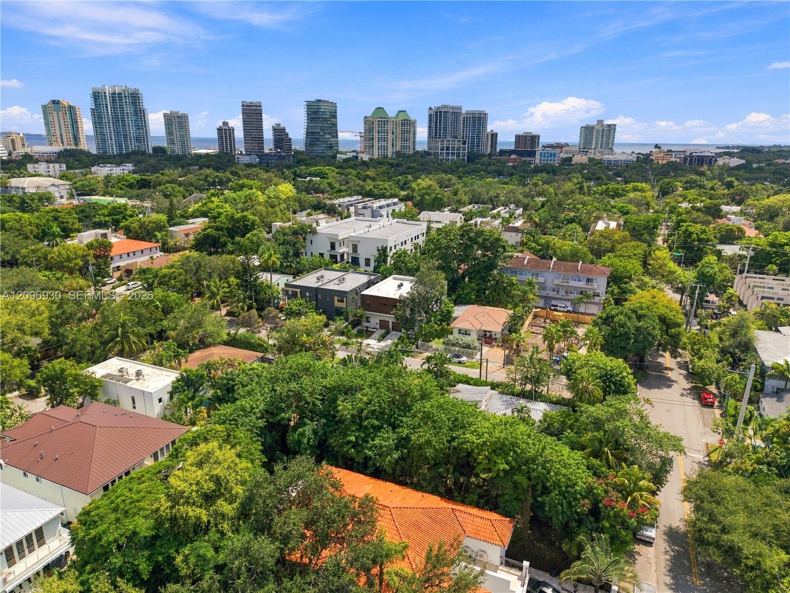 Aerial view over leafy Miami homes toward the waterfront and high-rise skyline.