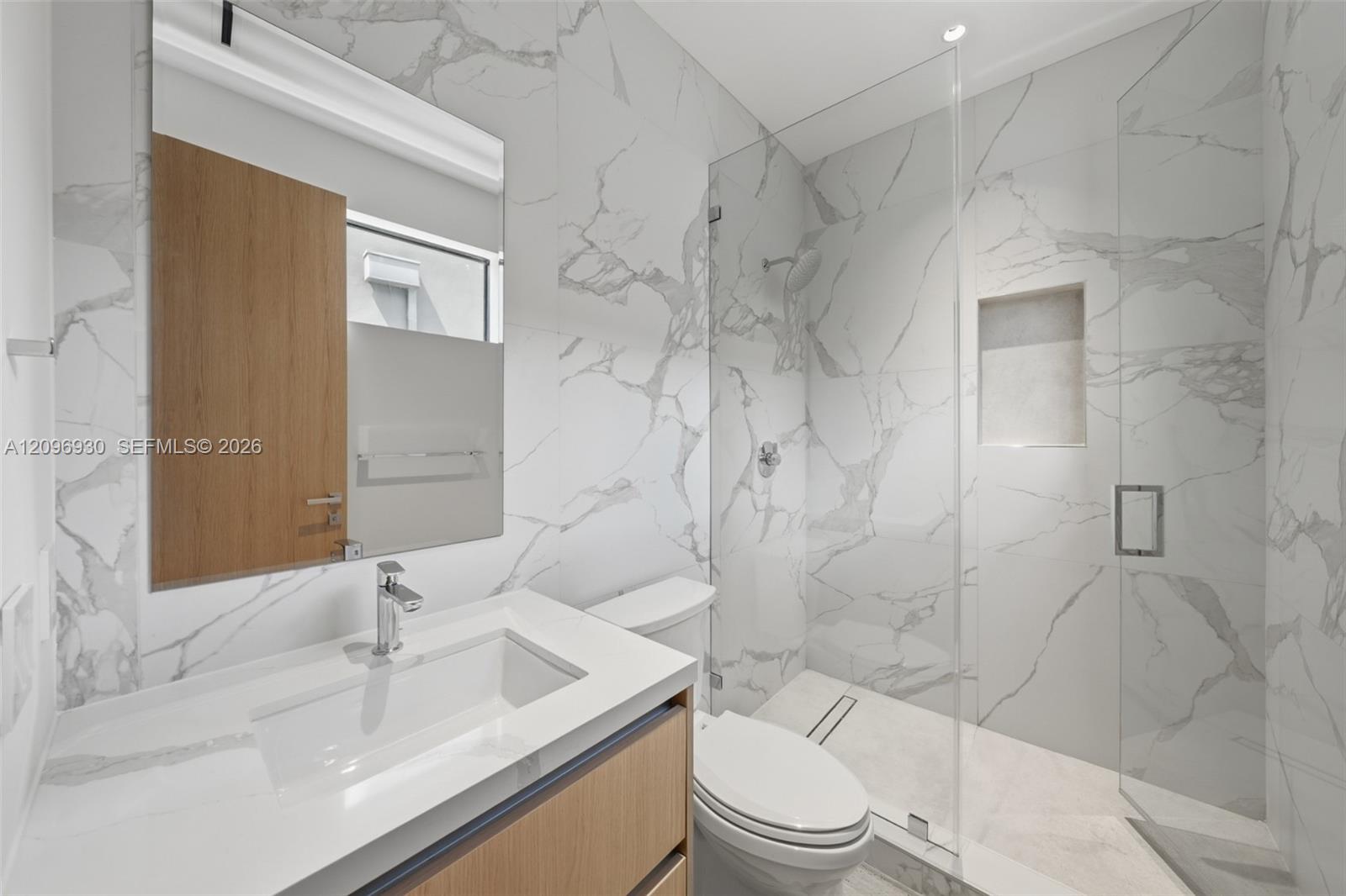 Modern bathroom with veined marble-look tile, a wood-front vanity, and a glass-enclosed shower.