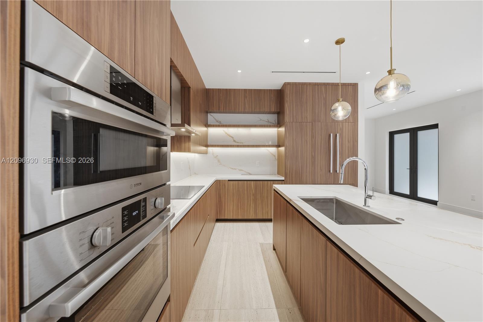 Modern kitchen with warm wood cabinetry, marble-look surfaces, stainless steel ovens, and a large island.