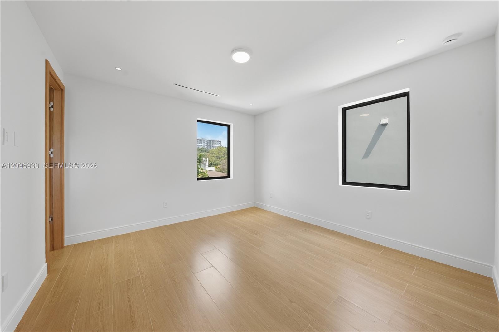 Empty room with light wood-look tile floors, recessed lights, and two black-framed windows.